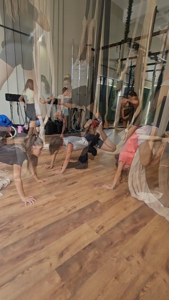 Indoor gym training session with multiple participants practicing aerial silks and floor exercises, image is blurry with motion effects.